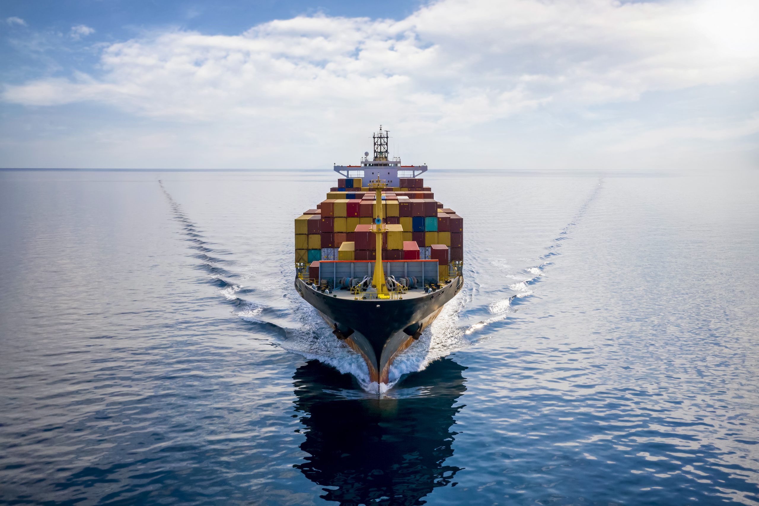 Aerial front view of a loaded container cargo vessel traveling over calm ocean